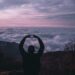 Man on a mountain with his hands over his head while his hands make a heart shape.